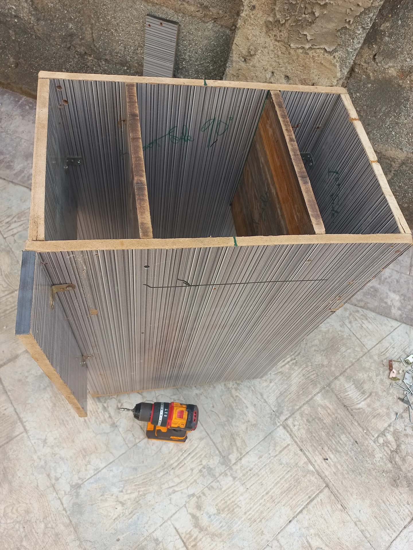 Elevated angled view of the bin showing the two upper sorting compartments open at the top and the structural framing at the front, with a drill on the ground