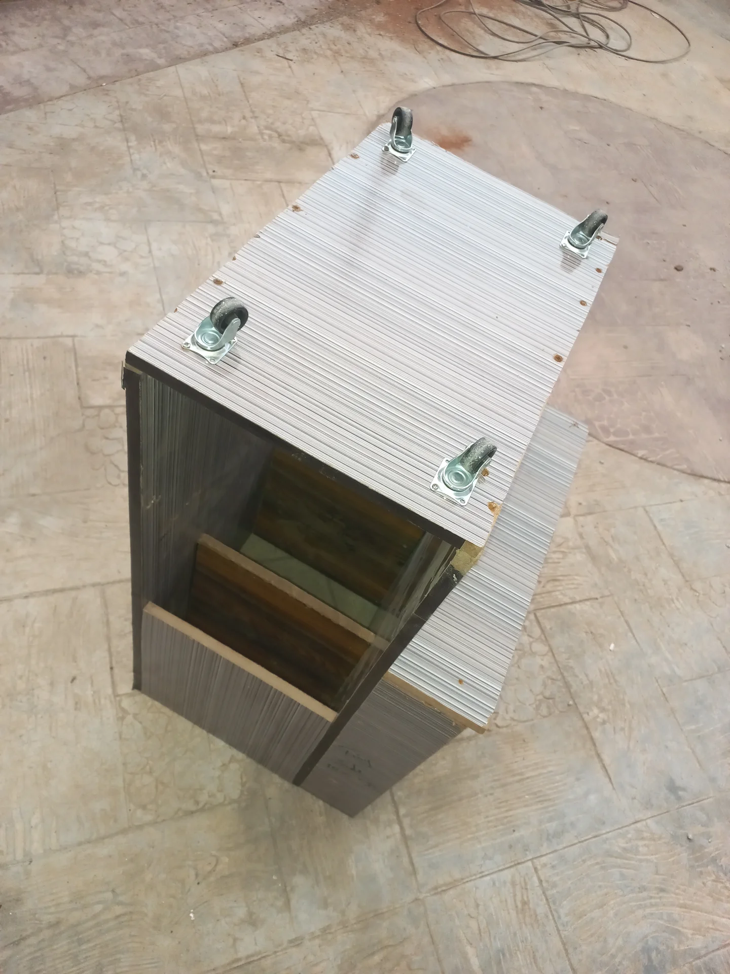Elevated view of the bin flipped upside down, showing the four castor wheel brackets mounted on the base panel, with the interior visible through the open front