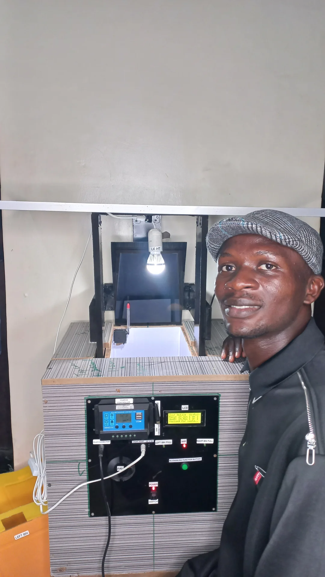 Builder standing beside the powered-on finished system, with the sorting chamber light visibly on and the electronics panel face showing