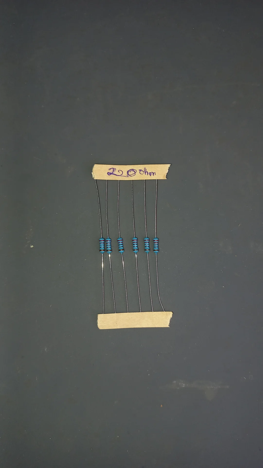 Five 220 ohm metal-film resistors held between two cardboard strips with the value handwritten as 220 ohm, used as LED current limiters