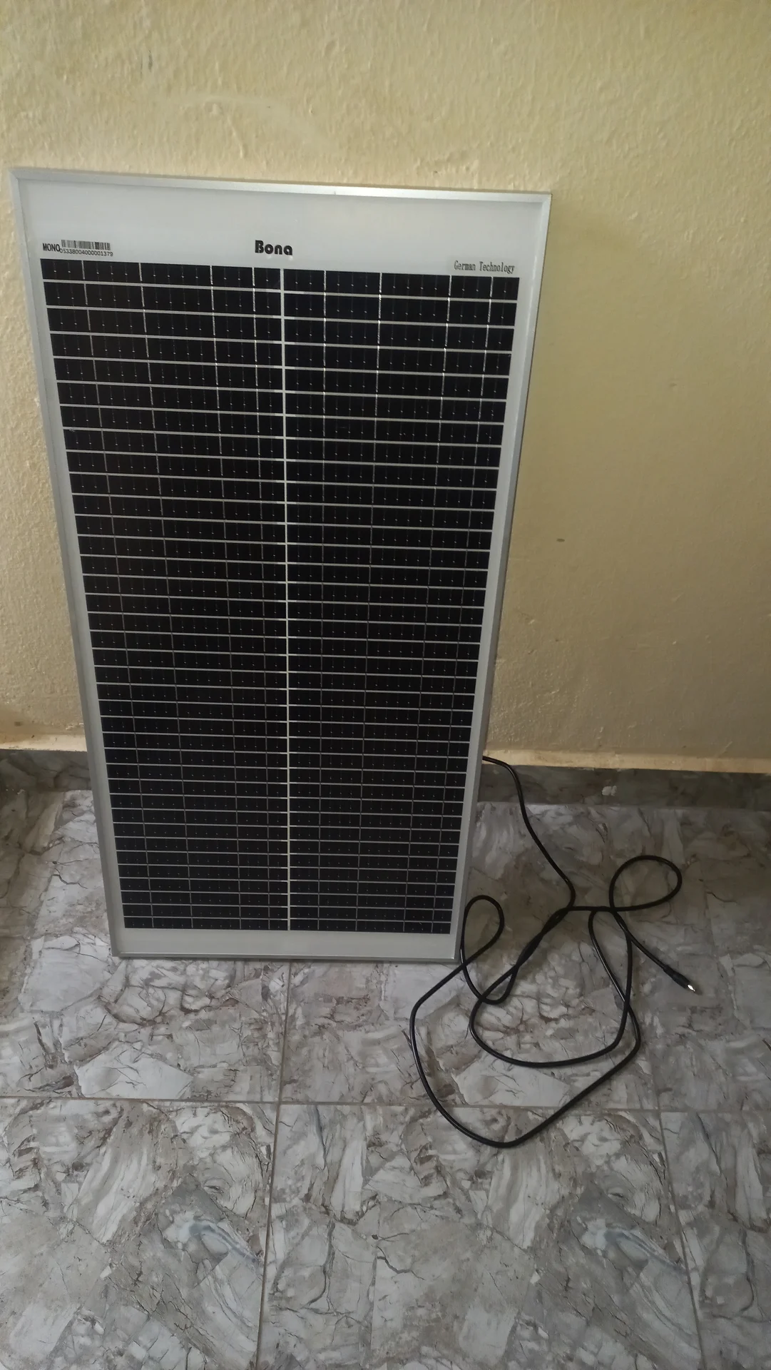 The 50 W Bona solar panel propped upright against a wall, showing its full face and the cable coiled at the base