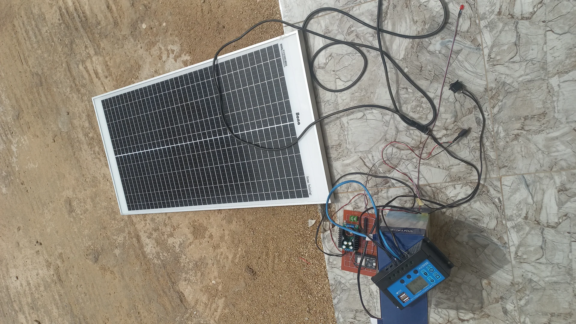 Top-down view of the outdoor power-system test with the solar panel, battery, charge controller and additional electronics on the ground