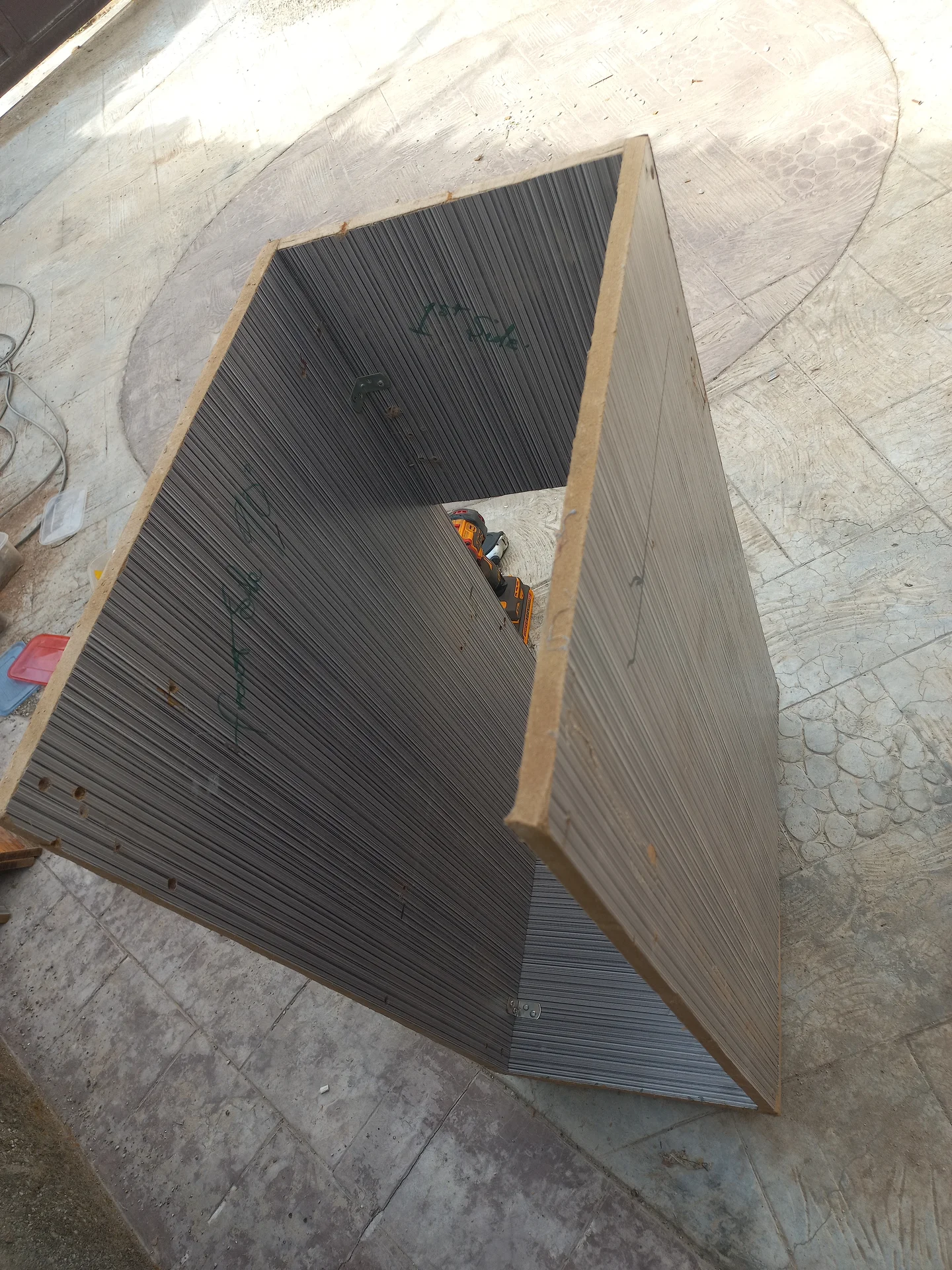 The bin body shell under construction showing the corrugated side and back panels joined with wooden framing, with a drill inside, photographed from above