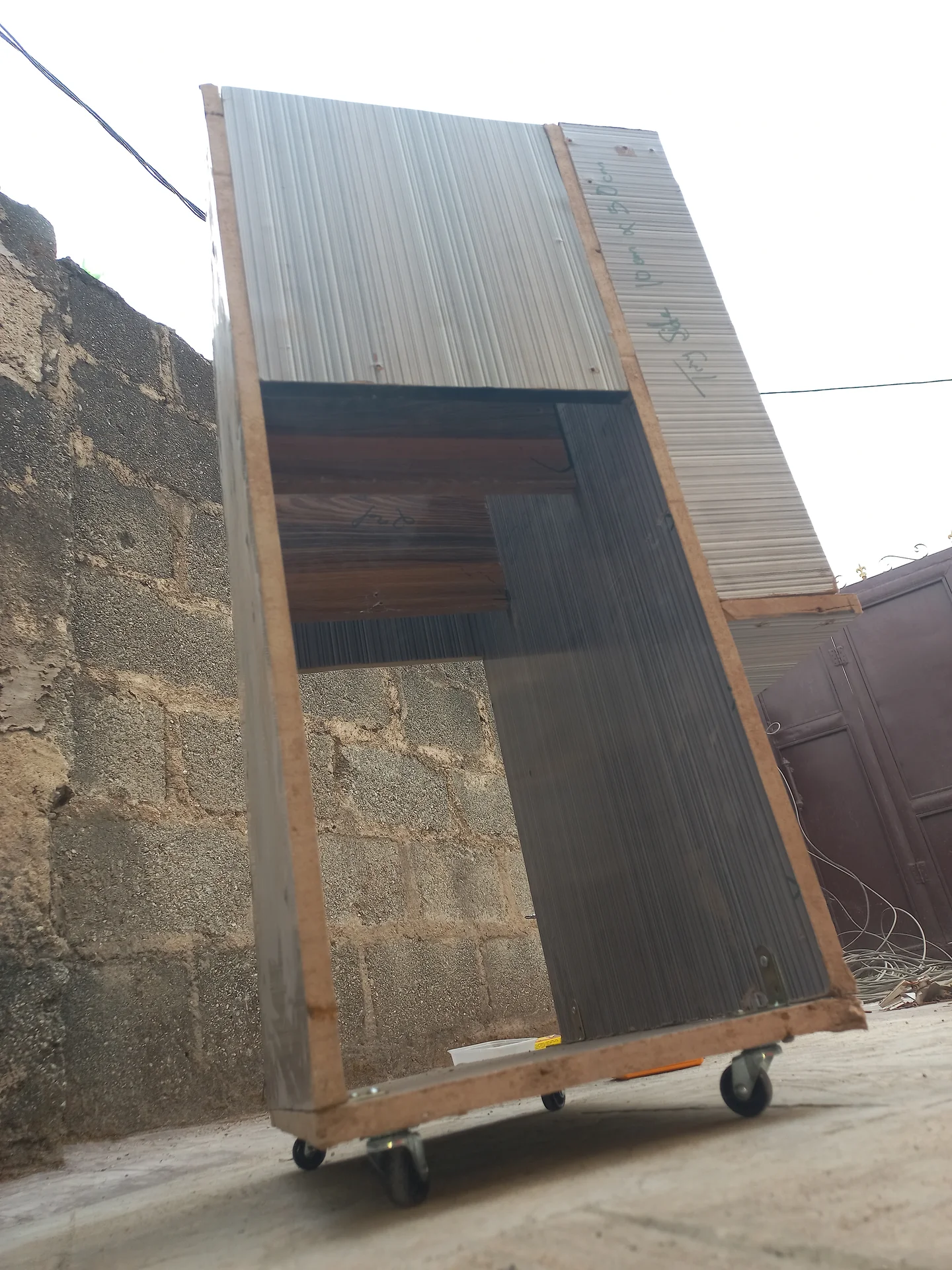 The bin frame tipped at a steep angle outdoors on its caster wheels, showing the corrugated side panels and the open interior from the side