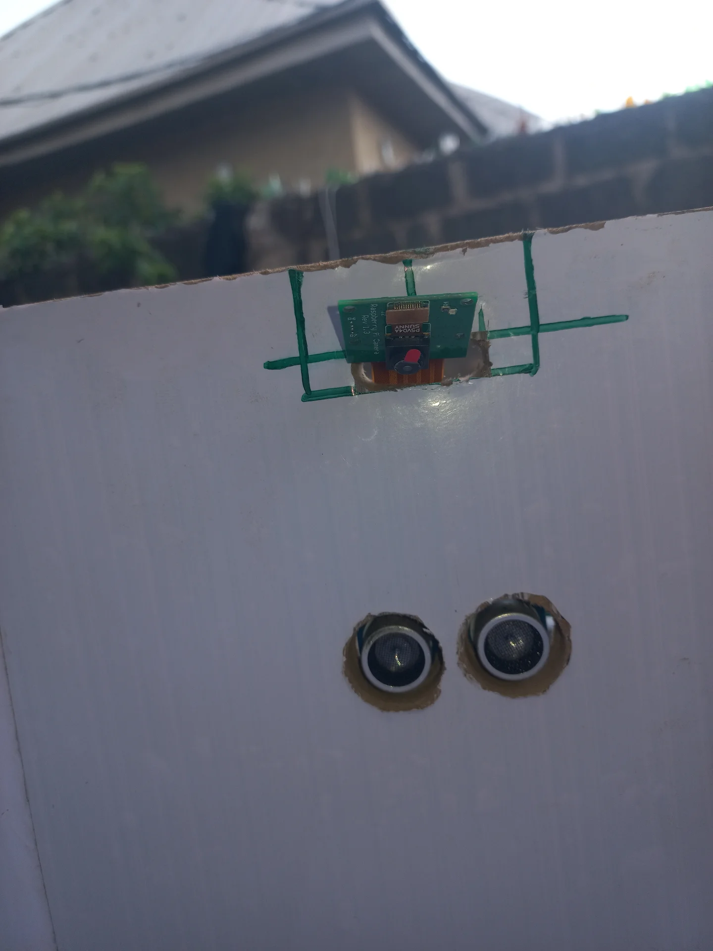 Exterior view of the bin wall showing the Pi Camera PCB mounted in its cutout at the top, with the two HC-SR04 ultrasonic sensor barrels mounted below it