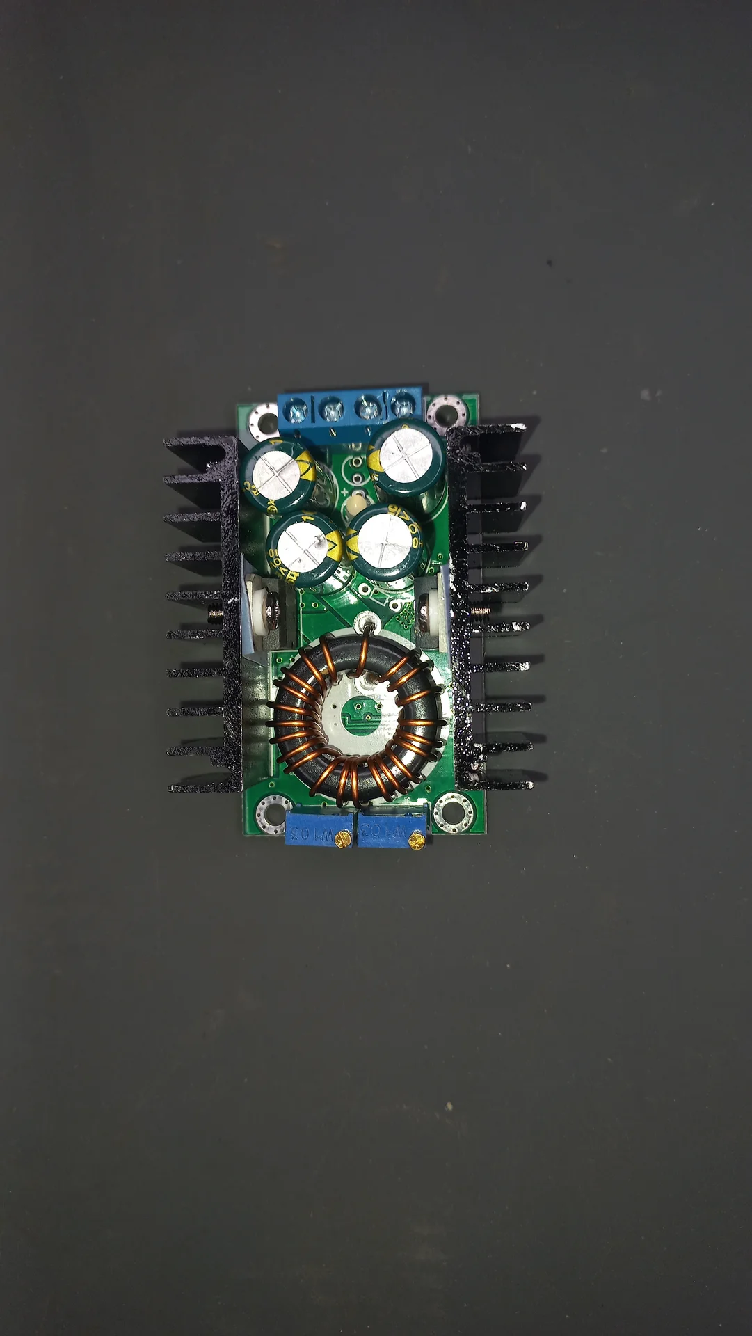 DC-DC buck converter with large toroidal inductor, multiple capacitors, blue screw terminal blocks and heatsink fins on both sides