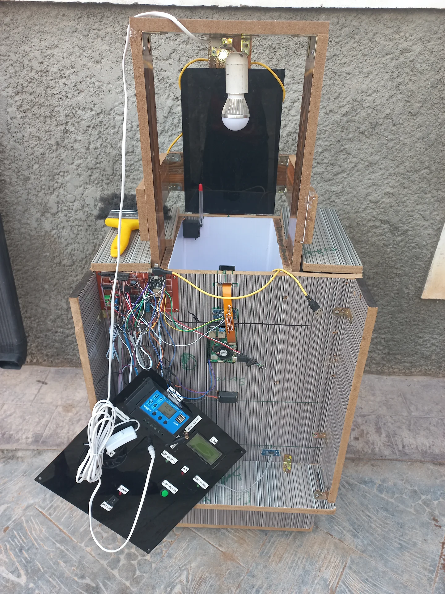 Front view of the assembled system outdoors showing the bin body, the open sorting chamber above with the interior light bulb on its frame, and the electronics panel face