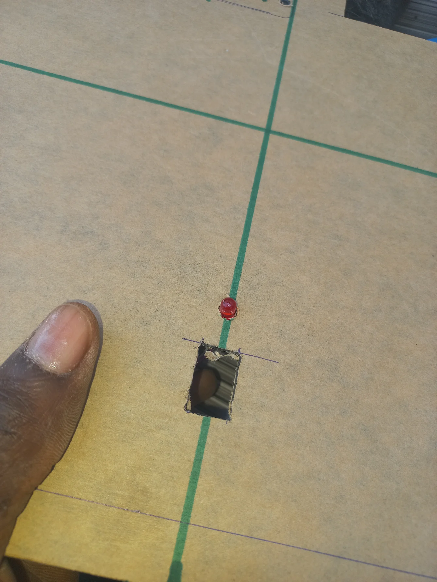 The panel board mid-process with a rectangular slot already cut and a button trial-fitted, showing the green marker layout lines