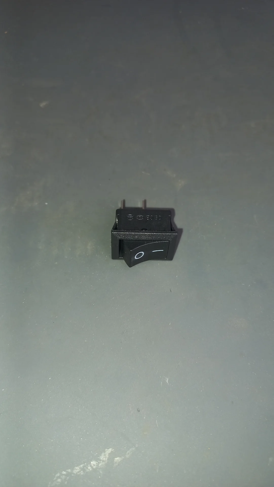 Mini rocker switch from the front showing the O/— on-off symbols and two connection pins