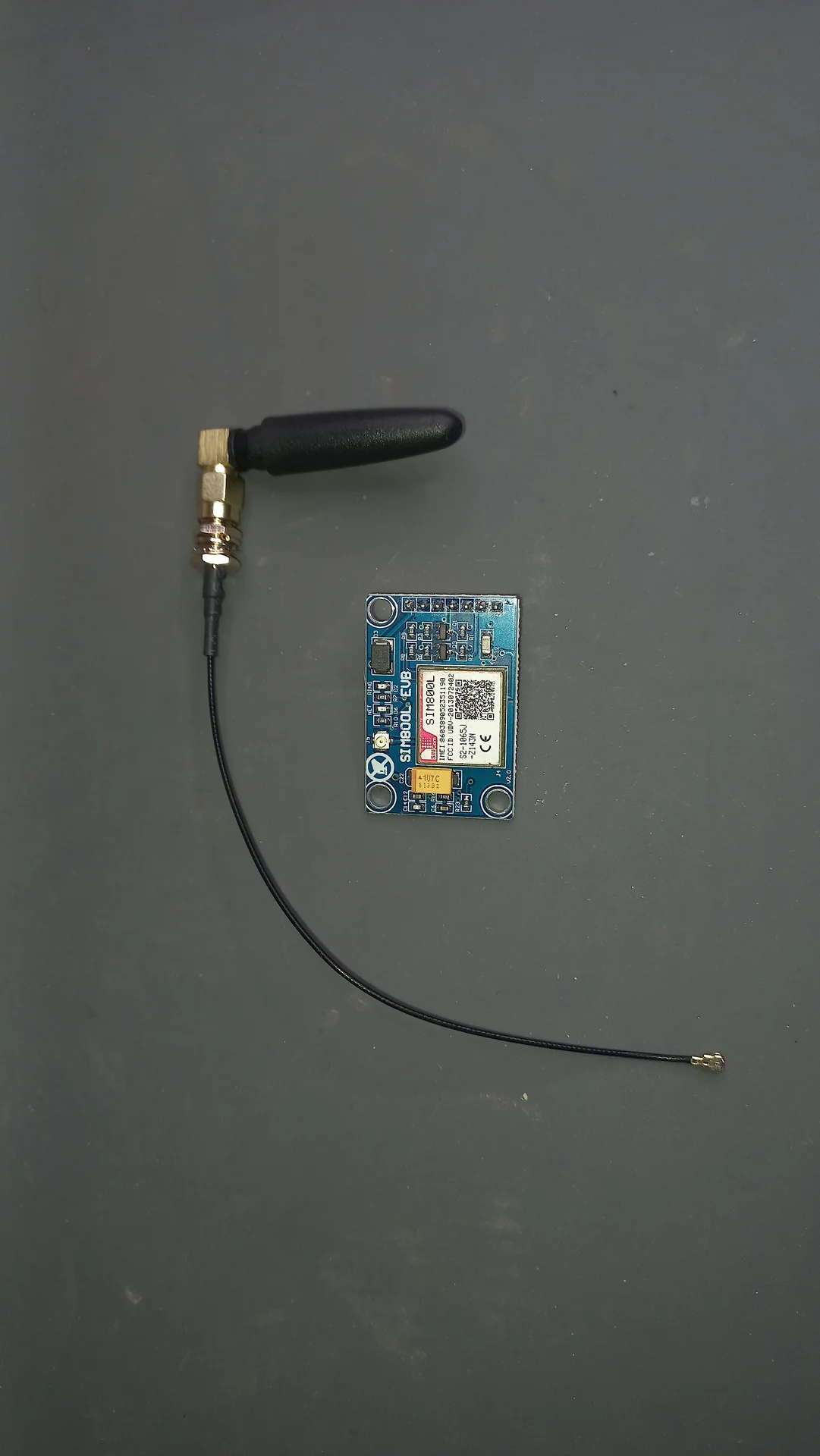 SIM800L GSM module (blue EVB board) with its external whip antenna connected via a u.FL coaxial pigtail, the component that sends SMS alerts