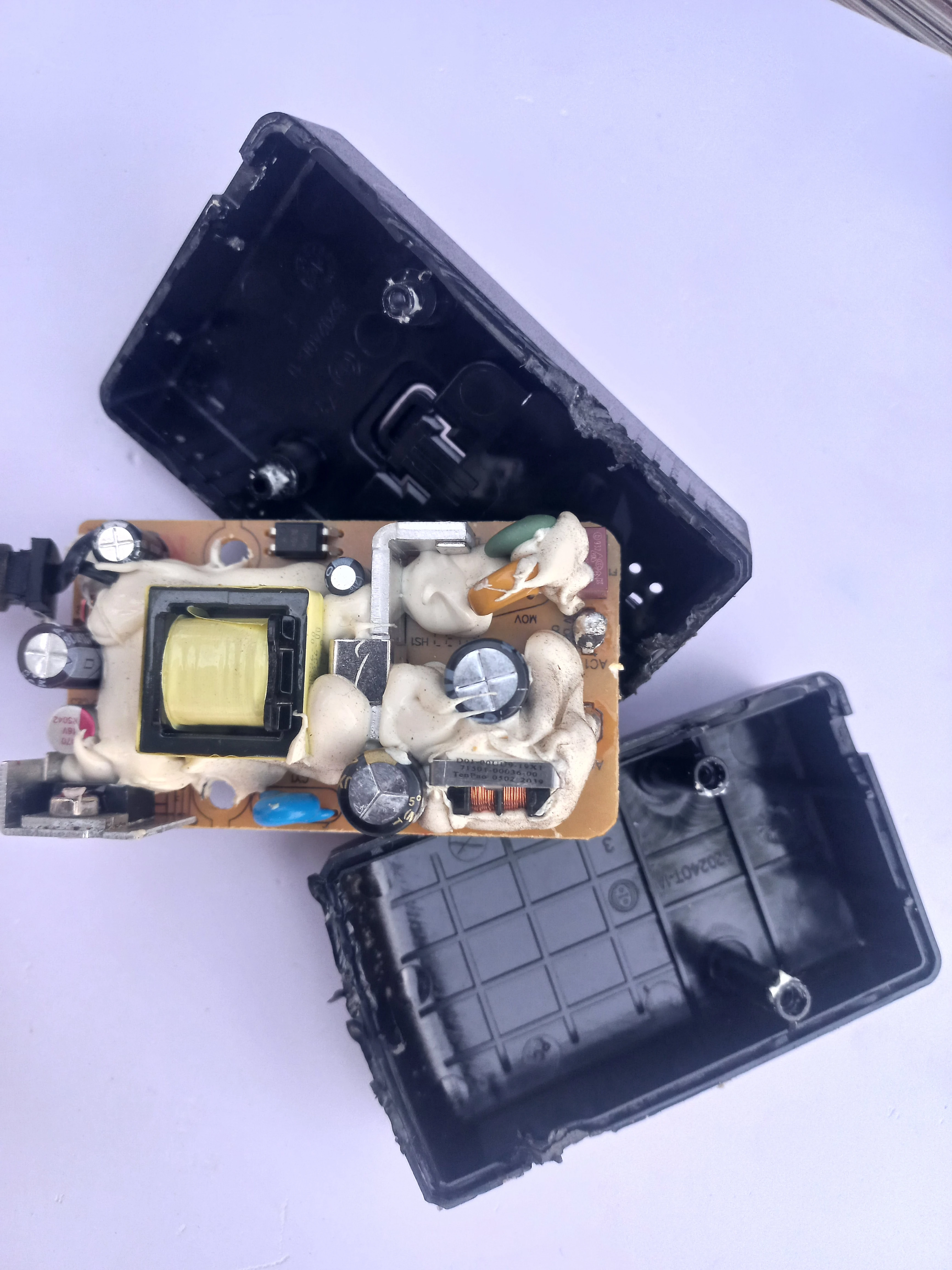 BT AC adapter opened and disassembled, showing the internal switching PCB and transformer